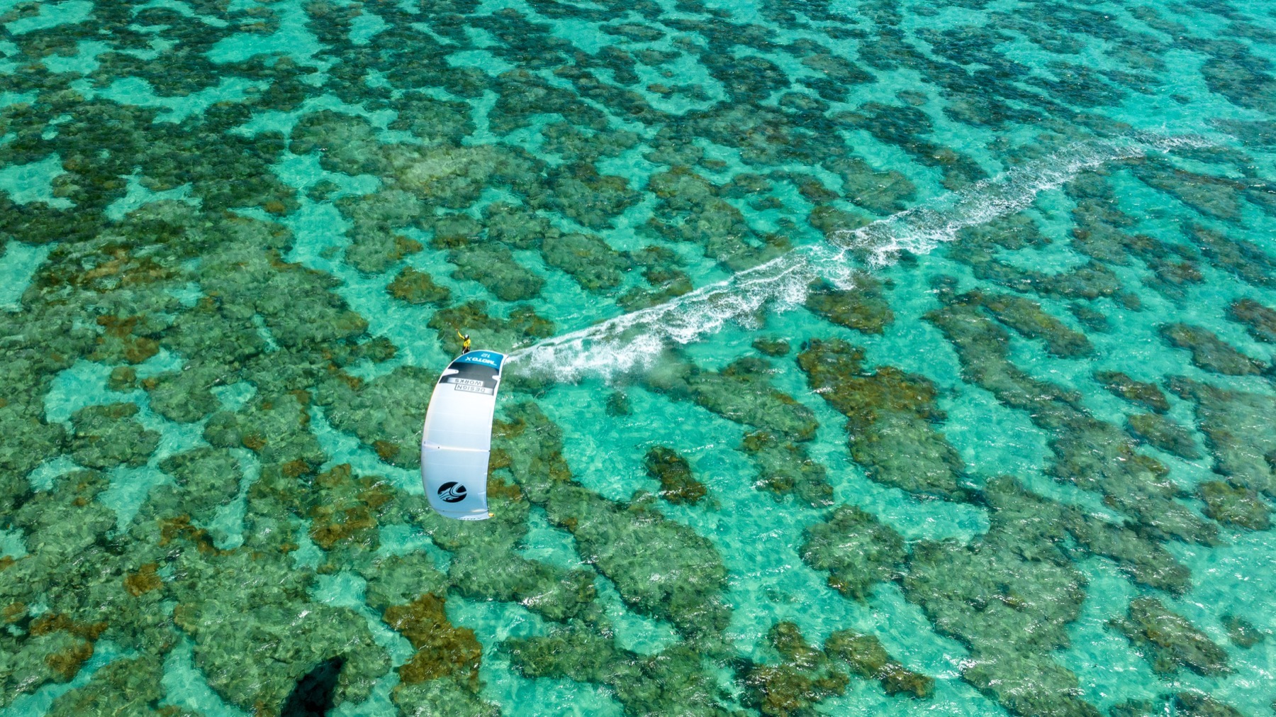 Vista aérea de Manu La Porta velejando de kitesurf entre recifes em água cristalina